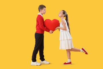 Cute little happy children with heart-shaped pillow blowing kisses on yellow background. Valentine's Day celebration