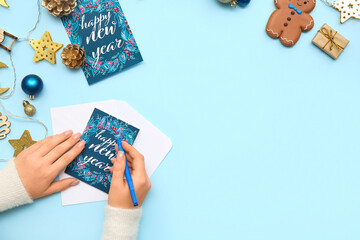 Female hands with greeting cards, pen and beautiful Christmas decorations on color background