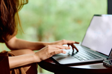 Young woman typing on a laptop, showcasing creativity and focus, in a cozy caf with a blurred green...
