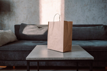 Disposable bag of kraft paper with products left by courier of food delivery service on a table at home. Copy space. Kraft design. High quality photo