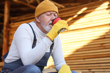 Mature male carpenter with cup of coffee sitting at sawmill