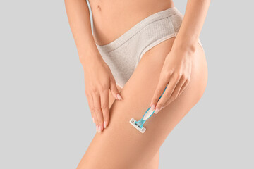 Beautiful young woman shaving legs with razor on grey background, closeup