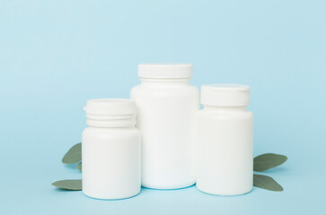 Bottles with pills and green leaves on color background