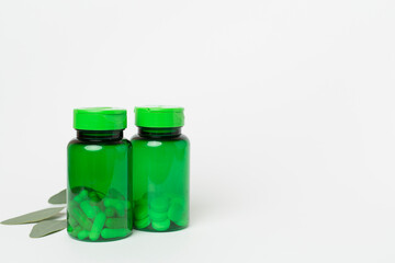 Bottles with pills and green leaves on color background