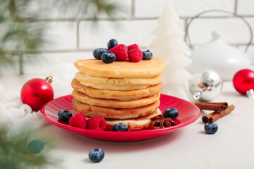 Plate of sweet pancakes with berries and Christmas balls on white table