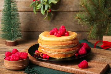 Plate of sweet pancakes with berries and Christmas tree on wooden background