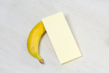 A ripe yellow banana and a bar of white chocolate are placed on a light wooden table, suggesting a...