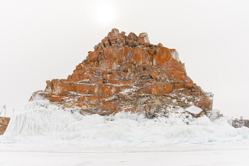 The sky is cloudy and the sun is setting, creating a moody atmosphere. View of Mount Shamanka, Lake Baikal in winter