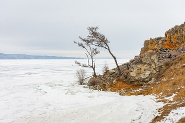 The sky is cloudy and the sun is setting, creating a moody atmosphere. View of Mount Shamanka, Lake Baikal in winter