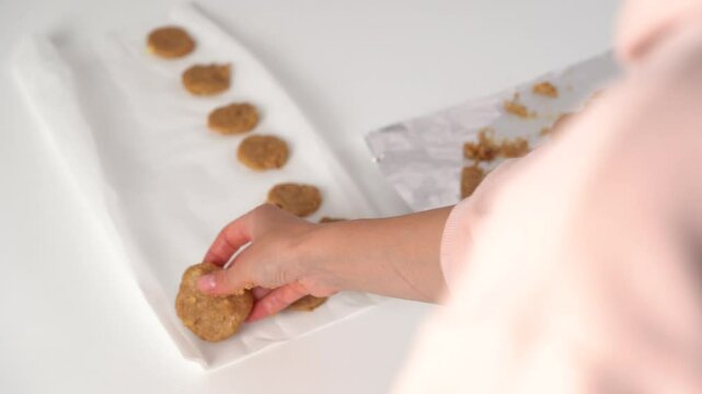 Close-up of young woman's hands forming round balls and spreading them on parchment for making cookies. Concept of ingredients for baking food at home, culinary hobby