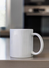Closeup of  white blank coffee mug on grey kitchen table over blured kitchen interior, mockup