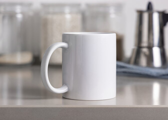 Closeup of  white blank coffee mug on grey kitchen table over blured kitchen interior, mockup