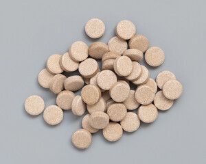 Pile of beige herbal pills on grey close up. Taking dietary supplements and vitamin