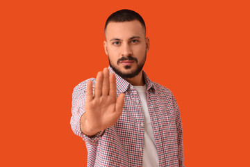 Young man showing STOP gesture on orange background. Rules concept