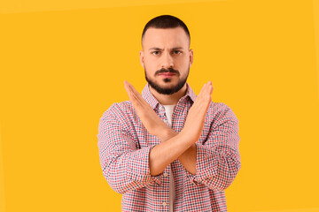 Young man showing STOP gesture on yellow background. Rules concept