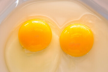 Detalhe de dois ovos crus dentro de um prato de louça branco. Fotografados de cima.