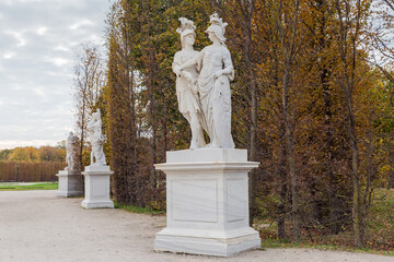 Garden alley with white stone sculptures in autumn park