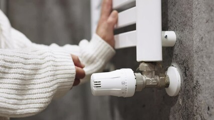 A hand adjusting the heating radiator as cold weather sets in, seeking warmth and comfort at home. A concept highlighting seasonal changes, home heating, and energy efficiency for winter.