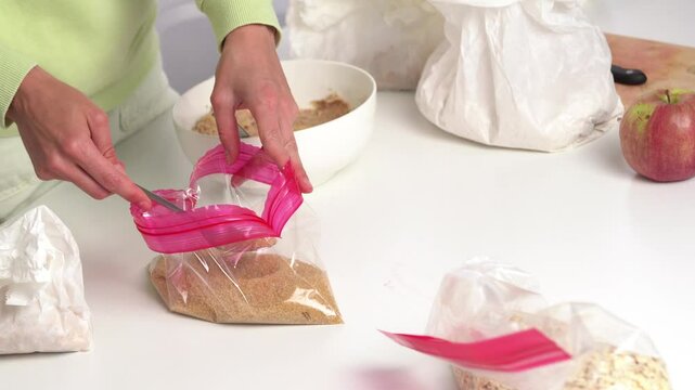 Young woman scoops brown cane sugar from a transparent zip bag and adds it with a spoon to a bowl with dough on the kitchen table. Concept of home baking, making pie according to a recipe, ingredients