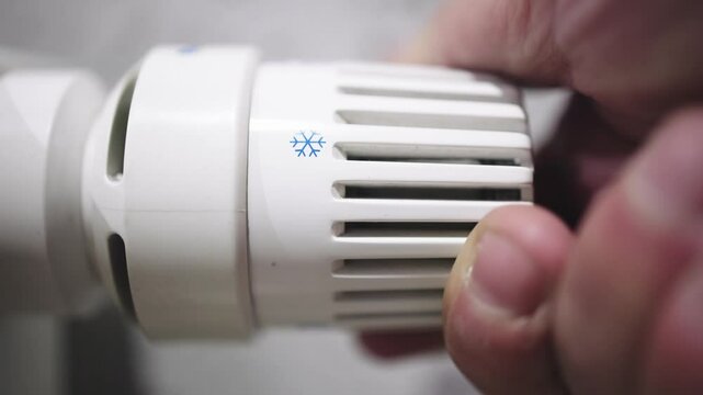 A hand adjusting the heating radiator as cold weather sets in, seeking warmth and comfort at home. A concept highlighting seasonal changes, home heating, and energy efficiency for winter.