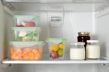 Concept of food preservation in the fridge. Fruits, vegetables in plastic containers and yoghurt and jam in jars. 