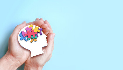 Hands holding paper head with jigsaw puzzle, Autism spectrum disorder family support concept, World...