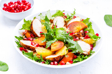 Winter persimmon salad with grilled chicken, pomegranate, walnuts, oranges and lettuce, white background, top view