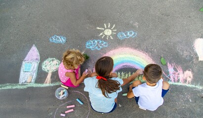 Children draw a picture on the asphalt with colorful chalk.