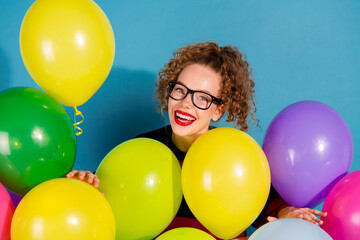 Obraz premium Young woman with curly hair and glasses surrounded by colorful balloons against a blue background