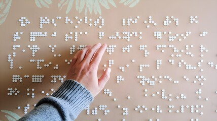 A blind person's hand caressing the relief while reading some braille letters. Make room in the copy for the editor's content.