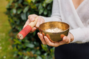 A hand holding a gleaming metal singing bowl with a mallet wrapped in red fabric. Used in sound...