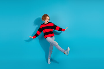 Obraz premium Charming young woman posing in a stylish striped sweater with a playful attitude on a bright blue background.