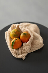 Three Tangerines In Mesh Bag On Table. Clementines, Satsumas, Mandarins, Oranges, Citrus With Green Leaf. Reusable grocery bag. Tangerine Mood. Home Atmosphere. Zero Waste Concept. Fruit Concept.