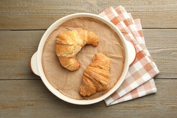 Ceramic casserole with croissants and baking parchment paper on wooden table, top view
