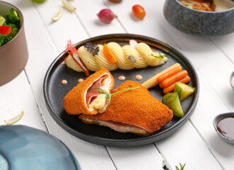 cordon bleu chicken With cheese and herbs, next to mashed potatoes, assortment of side dishes, white wooden background