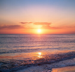 Obraz premium A serene sunrise over a calm ocean with gentle waves.