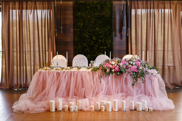 Newlyweds presidium decorated with pink tablecloth and a lot of candles, flowers. A modern banquet hall decorated with floristry. Wedding table decor, elegant table setting, beautiful interior.