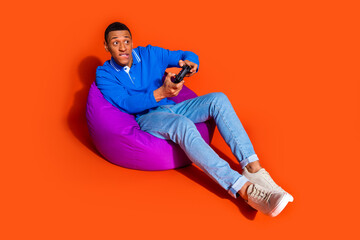 Young man playing video games on bean bag against vibrant orange background