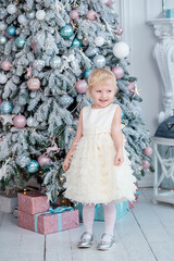 Elegant little girl decorates a stylish Christmas tree in a bright living room.