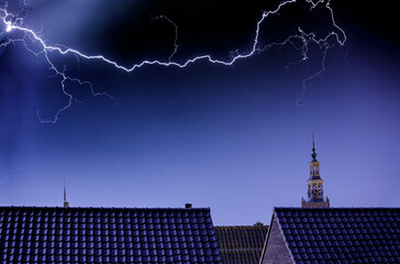 Dramatic lightning storm over rooftops and a historic clock tower.  Dark, moody scene.