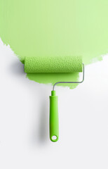 Fototapeta premium Green paint roller loaded with pastel green color isolated on a white background, top view, copy space. Diy creative concept of decoration, renewal and transformation of interior.
