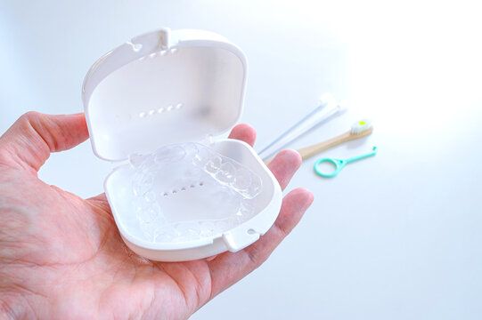 Estuche con alineadores dentales transparentes en palma de la mano, accesorios invisalign en superficie blanca.