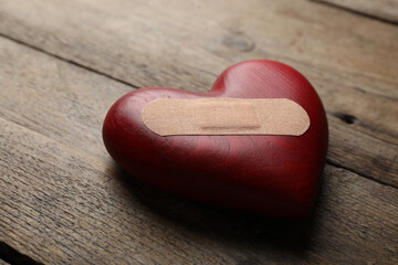 Heart with medical patch on wooden table, closeup. Relationship problems concept