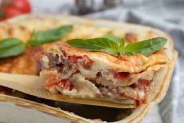 Taking piece of delicious cooked lasagna with basil at table, closeup