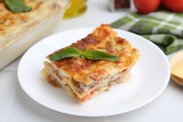 Piece of delicious cooked lasagna with basil on white table, closeup