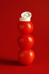 Stack of fresh tomatoes with plastic cap as bottle of ketchup on red background