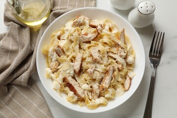 Tasty Alfredo pasta with chicken served on white marble table, flat lay