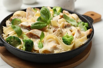 Delicious pasta Alfredo with chicken, cheese, creamy sauce, broccoli and basil on white table, closeup