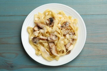 Tasty Alfredo pasta with chicken and mushrooms on light blue wooden table, top view