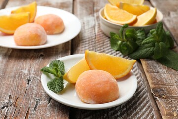 Plate with tasty mochi, cut orange and mint on wooden table, closeup